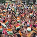 Large group of women at a patriotic ra;;y, actively waving small flags and holding hands
